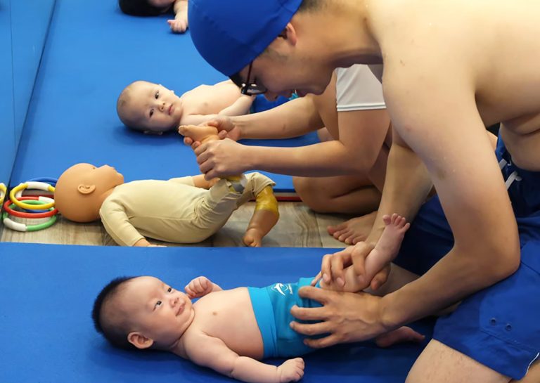 爸爸依照教練指導,為寶寶進行岸上嬰兒按摩 (infant massage),協助伸展嬰兒四肢,為下水前的肌肉喚醒做準備。