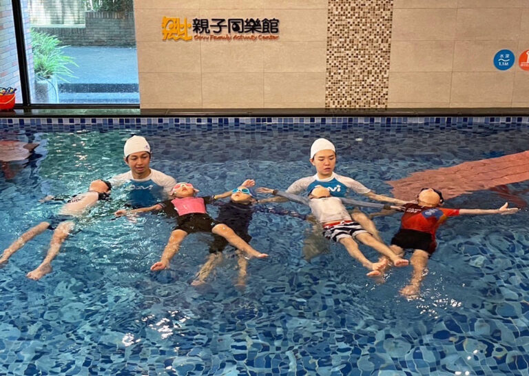 在穿著 Oovi 制服的教練指導下,兒童集體練習仰漂 (Back Float),訓練核心肌群控制與水面放鬆技巧,確保游泳過程中的安全性。