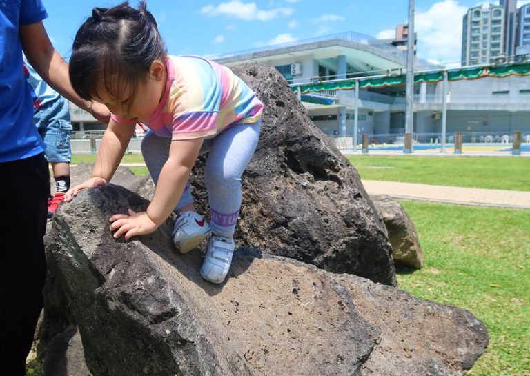 幼兒嘗試攀爬天然岩石,這項非結構化遊戲 (Unstructured Play) 能讓腳底適應不規則表面,刺激前庭覺與本體感覺,訓練真實環境下的平衡適應力。