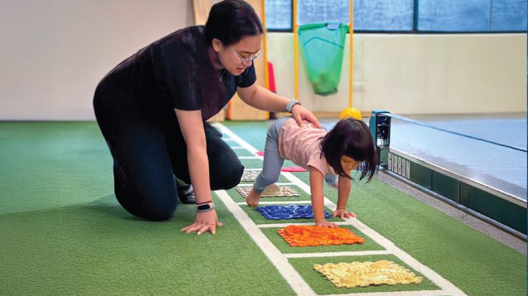 幼兒在指導下爬行通過觸覺地墊 (Sensory Mats)，這項感覺統合訓練能有效刺激手腳神經發展，並強化核心肌群與粗大動作 (Gross Motor Skills)。