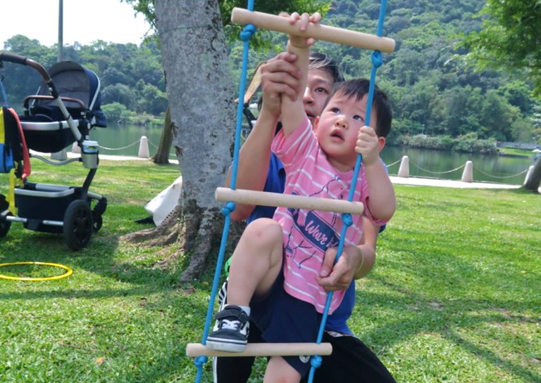 幼兒在戶外自然環境中挑戰軟式繩梯攀爬,這項活動能強化上肢肌耐力與抓握力,並透過克服高度恐懼建立自信心與冒險精神。