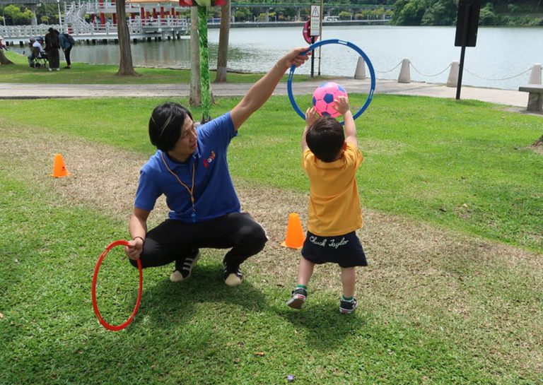 教練在戶外手持圓環作為目標,幼兒練習將球投入圈中,這項活動專注於訓練物體操控 (Object Control) 與空間距離判斷,強化手眼協調能力。