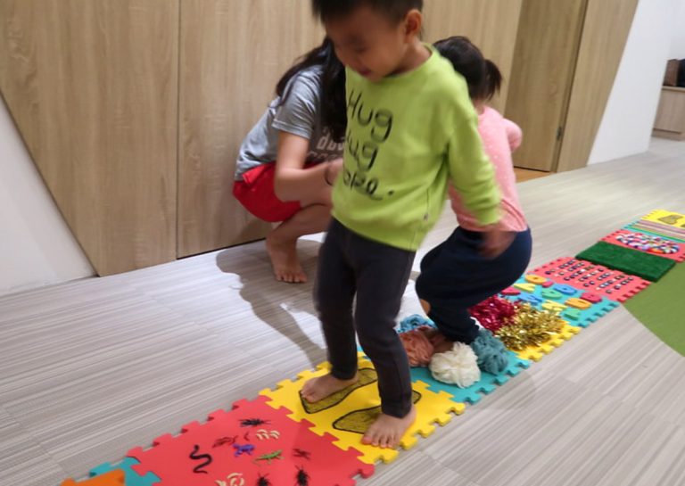 幼兒赤腳行走於不同紋理的觸覺步道 (Sensory Path),這項感覺統合訓練能直接刺激足底神經,促進大腦對觸覺的整合能力,並強化行走時的平衡穩定度。