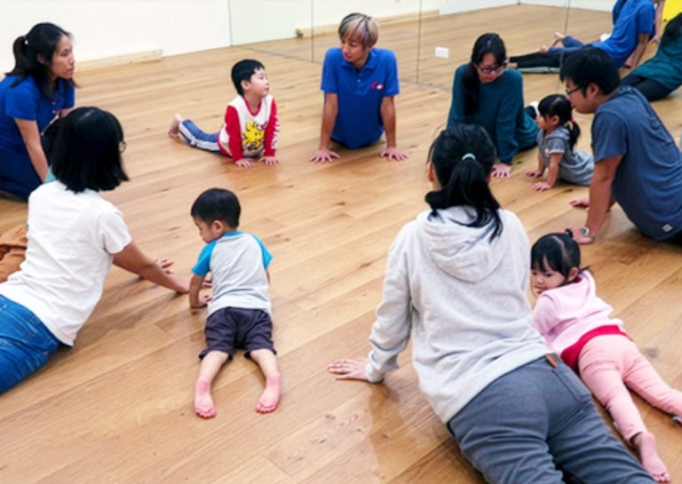 老師帶領兒童圍圈進行兒童瑜珈 (Kids Yoga) 的眼鏡蛇式伸展,透過動作模仿訓練背部肌群與核心力量,並在靜態活動中培養孩子的情緒穩定與專注力。
