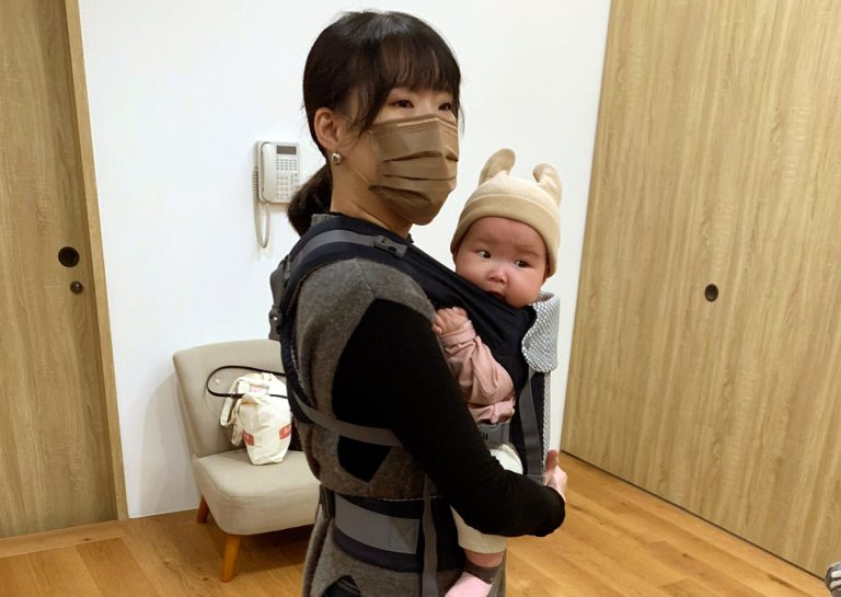 媽媽示範揹巾穿戴後的安全檢查重點,確保寶寶頭部貼近親吻距離 (Close enough to kiss) 且呼吸道暢通,展現正確穿戴對於預防嬰兒髖關節發育不良 (DDH) 的重要性。