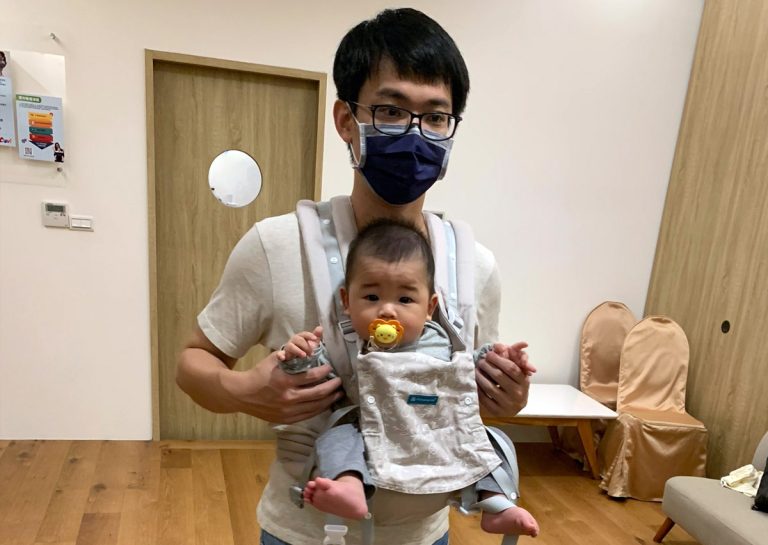 爸爸使用插扣式揹巾 (SSC) 面外揹寶寶,寶寶腿部呈現標準的 M字腿 (M-Shape) 健康坐姿,保護髖關節發育。這張照片鼓勵爸爸參與育兒,面外揹讓寶寶探索。