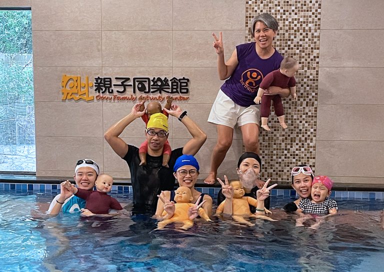 Oovi 親子同樂館專業教練團與培訓學員在泳池內開心合影,背景為 Oovi Family Activity Center 標誌。教練們使用專業教具娃娃進行水中模擬練習,展示 Birthlight 英國生之光 國際認證師資的嚴謹培訓流程與團隊熱忱。