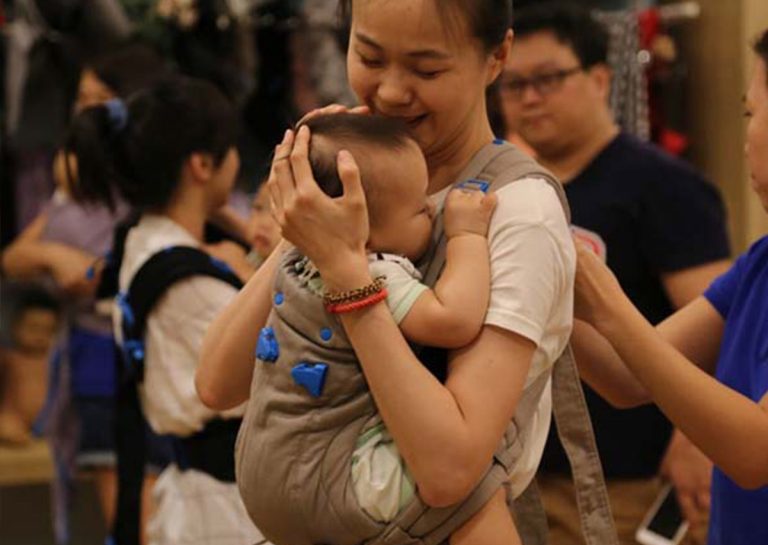 媽媽在揹巾中溫柔擁抱並親吻寶寶額頭,完美詮釋 T.I.C.K.S. 安全守則 中的「親吻距離」,強調揹巾穿戴不僅是工具,更是傳遞愛與親密育兒 (Attachment Parenting) 的橋樑。