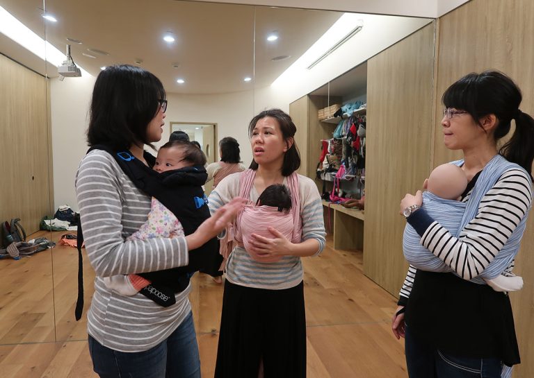學員們在 Oovi 教室透過大鏡子檢視揹巾穿戴細節,學習觀察寶寶姿勢與布料張力,這種視覺回饋 (Visual Feedback) 與團體互助的學習模式,能大幅提升家長操作的準確度與自信心。