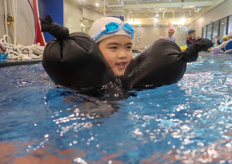 孩童在 Oovi 營隊中練習使用充氣救生包維持水面漂浮,透過模擬情境強化水域安全意識與應變能力。
