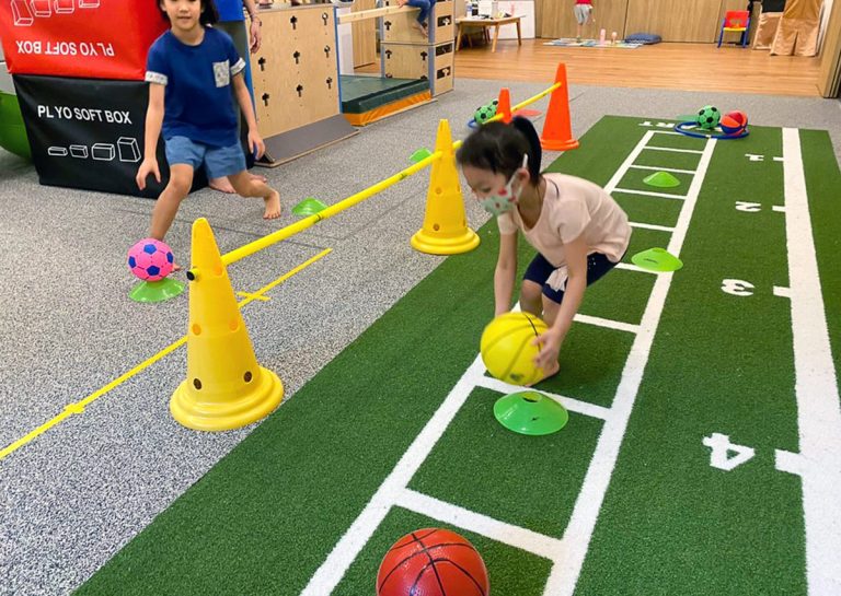 Oovi 暑假營隊學員在室內運動場進行球類運送挑戰,結合角錐障礙跑提升手眼協調與肢體反應力。
