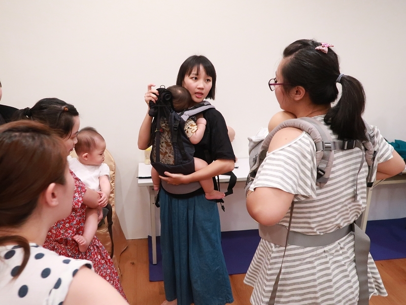 高雄揹巾輔導員小菜兒,揹著寶寶面帶笑容地示範揹巾穿戴